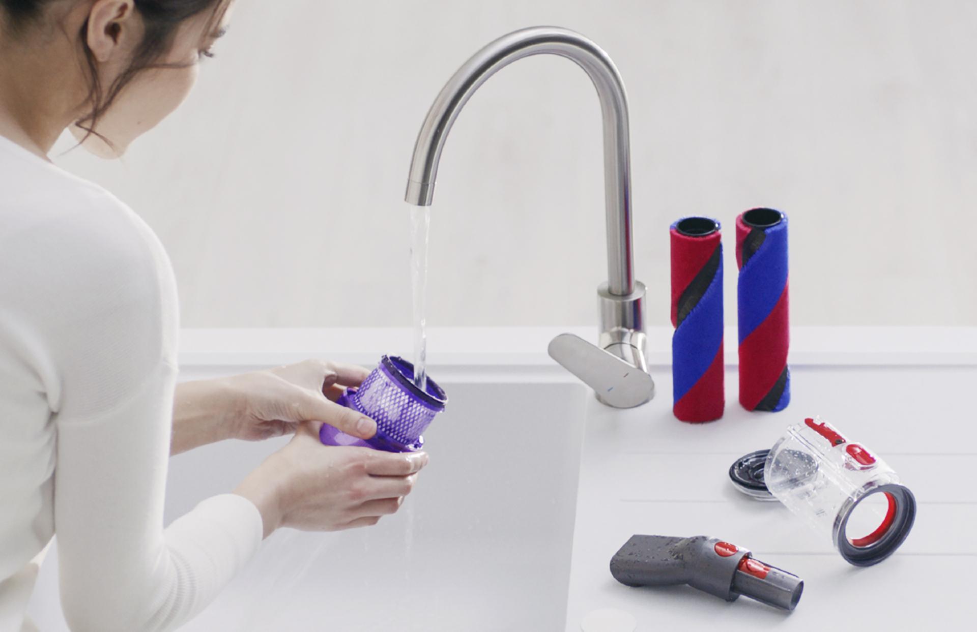 Woman washing vacuum parts under a tap.