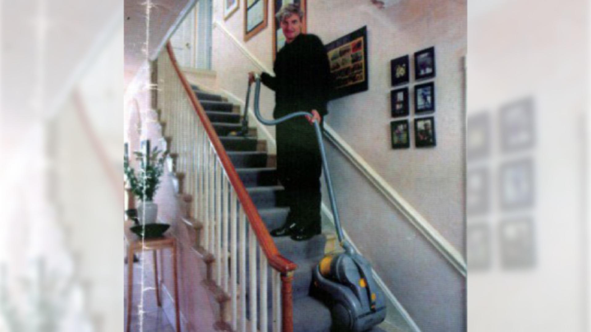 James Dyson standing halfway up the stairs, using the DC02 vacuum with ease