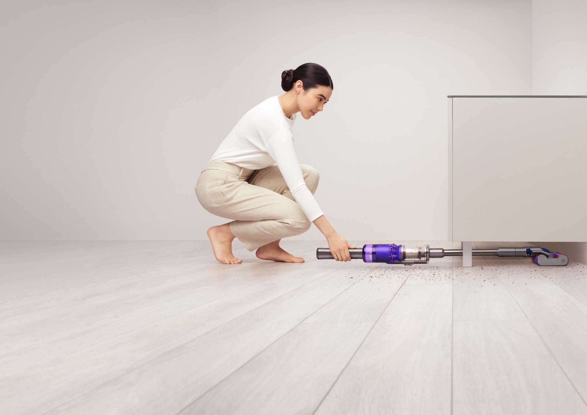 Woman using Dyson Omni-glide™ vacuum to clean under a cupboard.